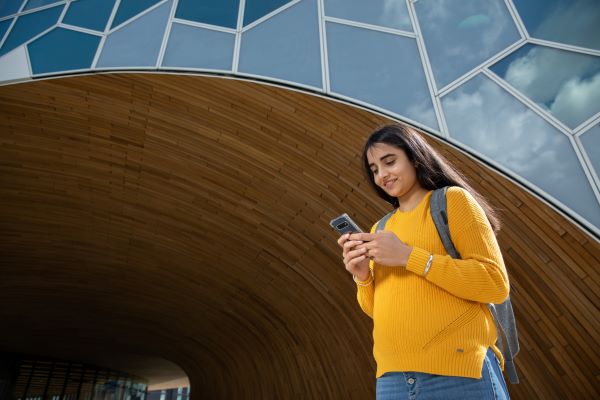 Student standing outdoors while using a mobile phone