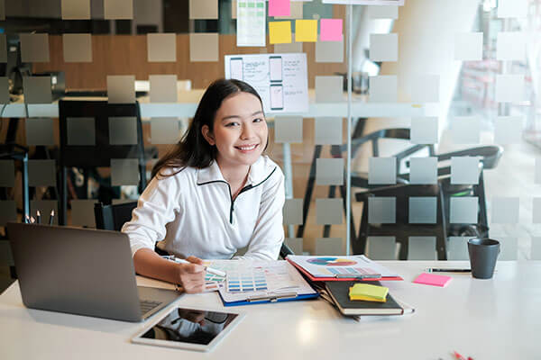 A woman sits at a desk, ready to help you with your writing skills.