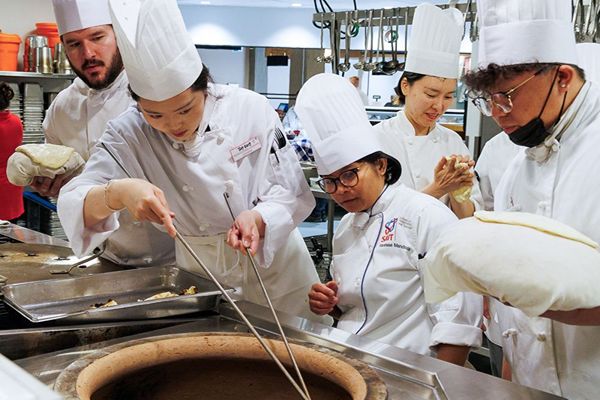 A group of culinary students in white chef uniforms and hats