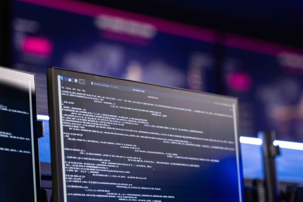 Close-up of a computer monitor displaying lines of code, with other monitors blurred in the background.
