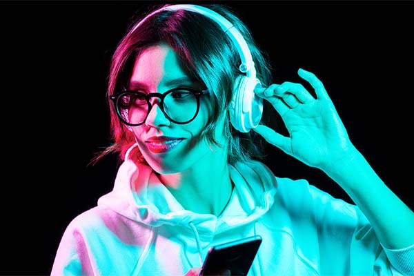 A young woman wears over the ear headphones. She's cast in red and blue light.