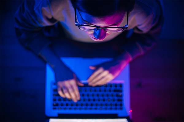 A person working on a laptop in low light, illuminated by blue and purple tones.