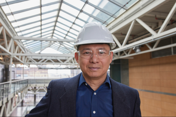 A man wearing business casual with a white construction hat, smiling at the camera.