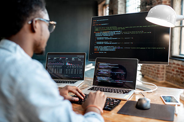 A programmer working on multiple screens, coding and analyzing data with graphs on the laptops.