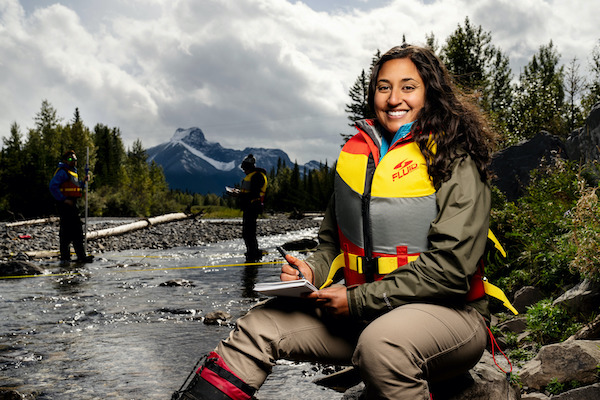 Person taking notes on a rocky riverbank during an outdoor field study.