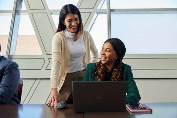 Two women engaged in a collaborative discussion at a laptop in a modern office setting.