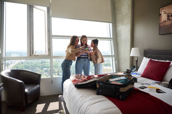 A group of students standing in the middle of a room while looking at a phone and smiling  