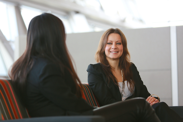 two professionally dress women smiling on couch