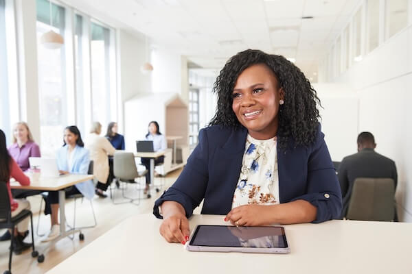 A women sits in an office area with a tablet on the table in front of her