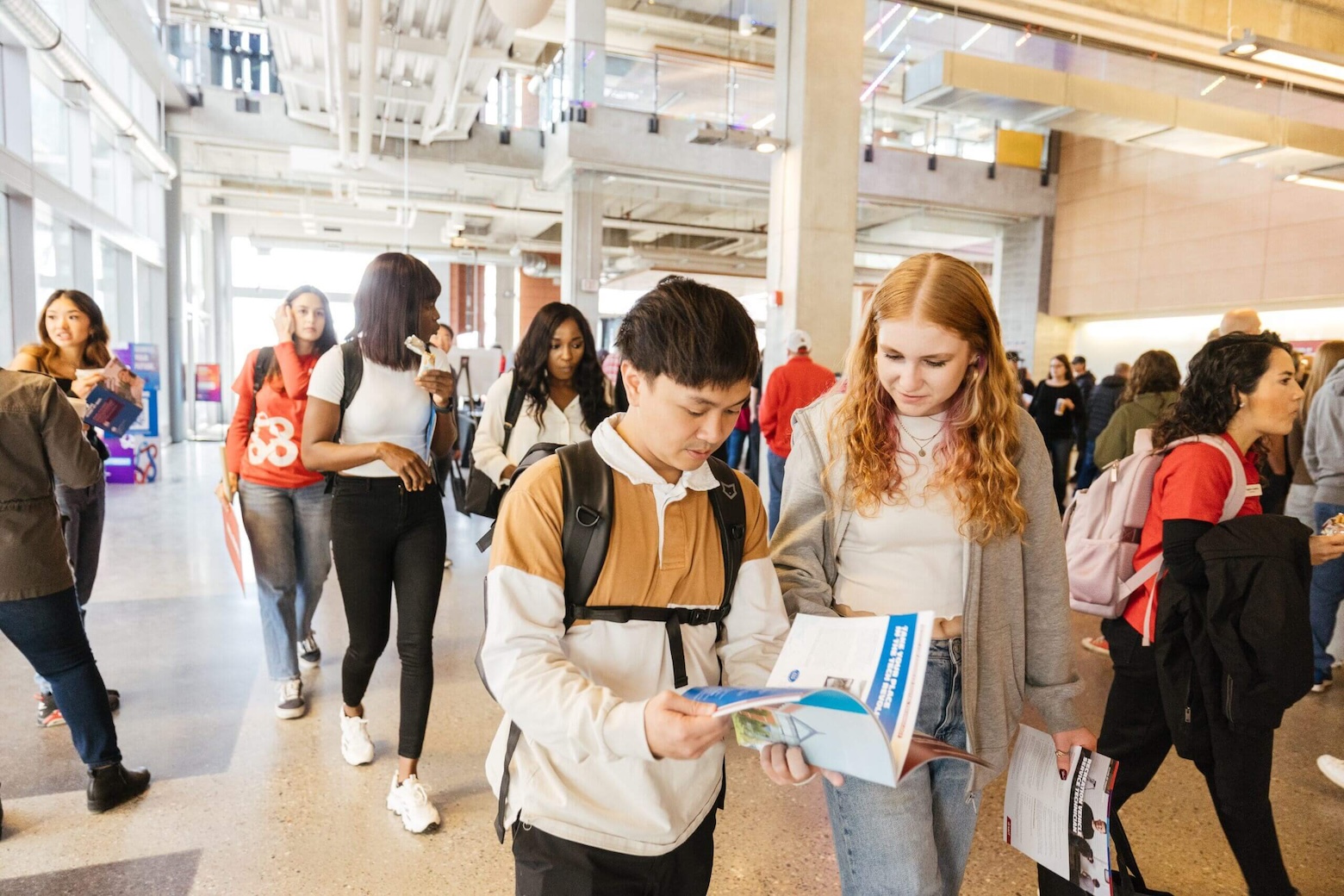 Students interacting and exploring a brochure in a busy campus hallway.