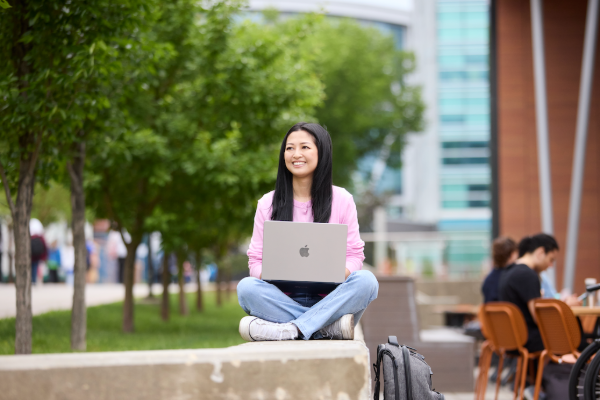 A student sits outside with a laptop.