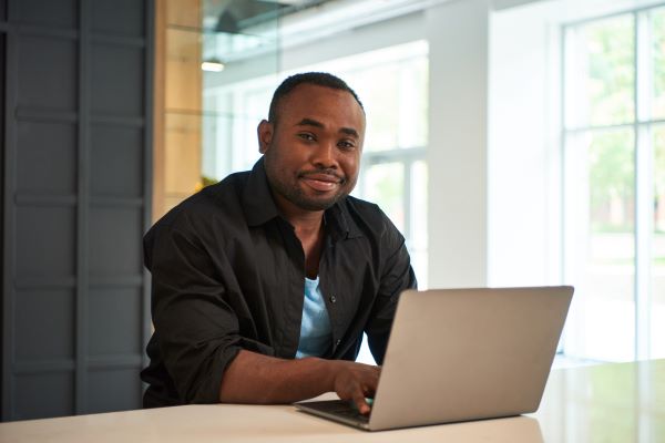 A man sitting using a laptop looking at the camera