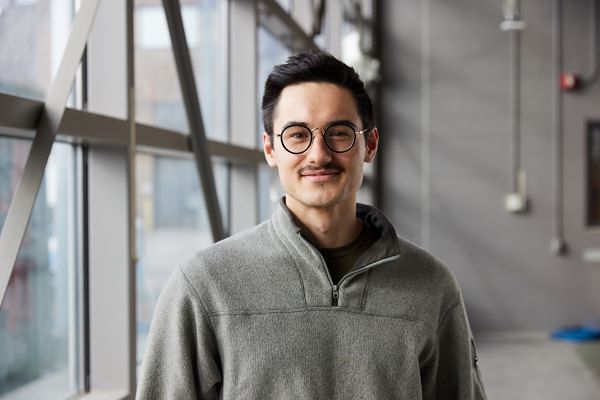 Person wearing a gray quarter-zip sweater standing indoors near large windows.