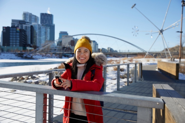 Student in downtown Calgary in the wintertime, holding out a phone.
