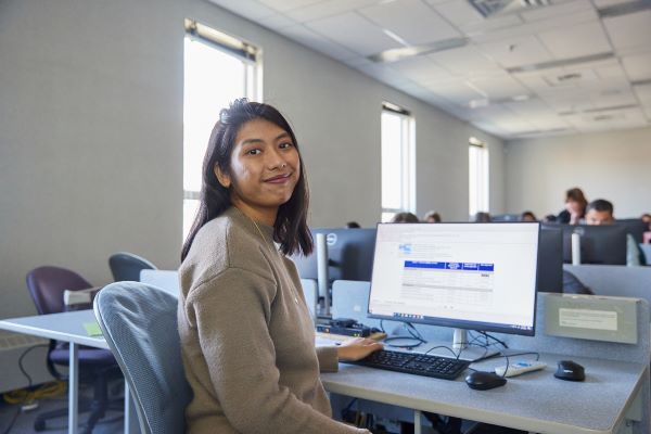 Student sitting at a computer smiles at the camera