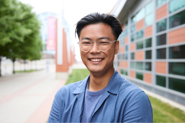 A student wearing glasses stands outside on SAIT campus, smiling in the summertime. 