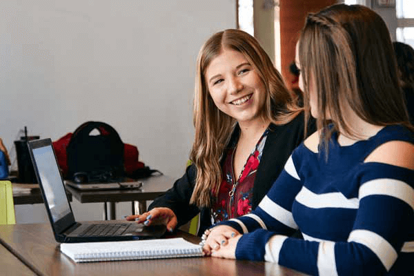 Two students sitting at a desk and talking with each other