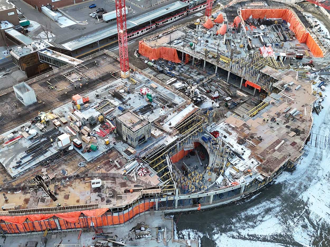 Aerial view of the Taylor Family Campus Centre construction site on Nov. 20, 2025, showing a large red crane, concrete superstructure, orange tarps and workers around the building, in progress.