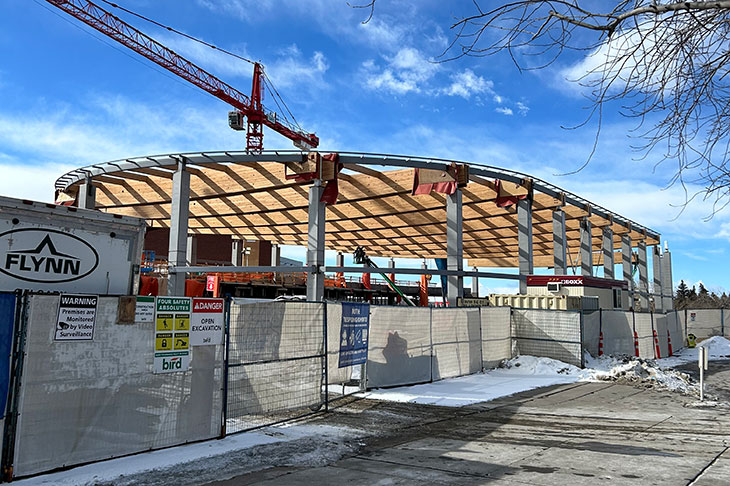 construction site showing mass timber beams being installed on cement pillars with a red crane in the background