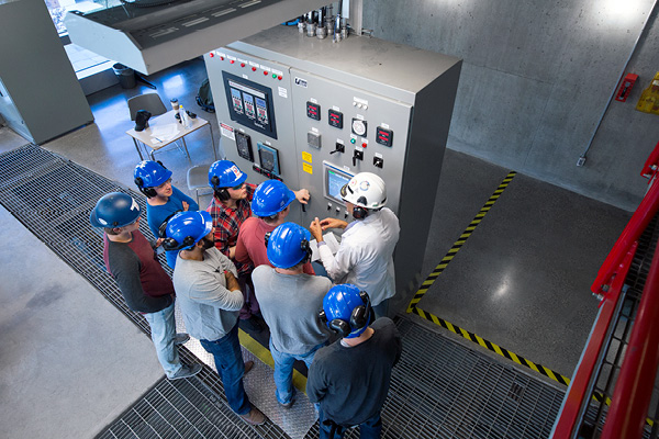 Students listening to an instructor in front of a control machine