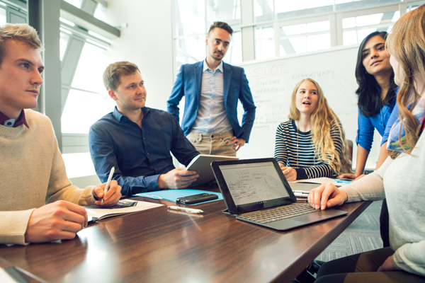 A group of diverse professionals engaged in a collaborative brainstorming session around a conference table, with notes and a laptop visible.
