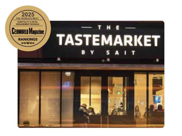 A modern restaurant exterior with large glass windows, featuring the name "The Tastemarket by SAIT." A gold badge indicates it is recognized in the 2025 CEOWORLD Magazine rankings for hospitality and hotel management schools.