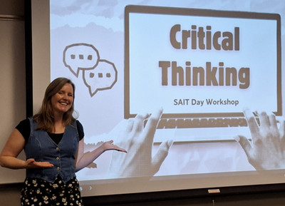Photo of Hilary Wallis standing in front of a big screen with her Critical Thinking presentation title slide.