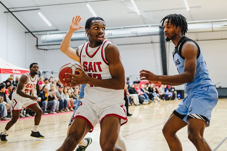 A basketball player from SAIT in a white jersey holds the ball.