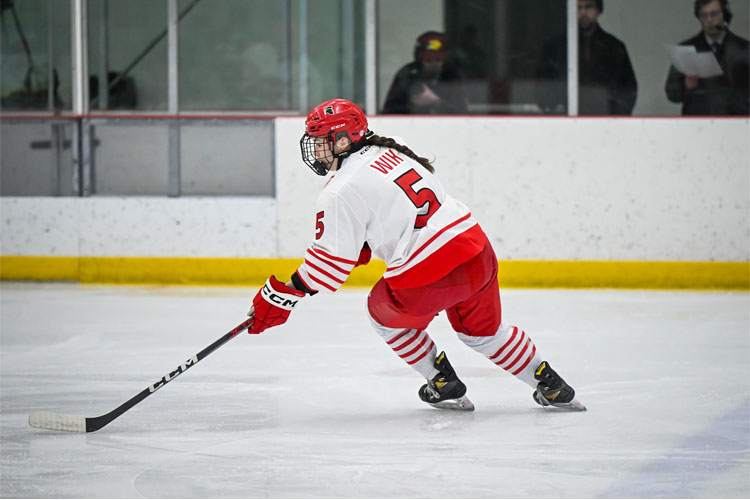 Trojans women's hockey player in a white-and-red uniform skating on the ice with a stick, number 5 visible on the back.