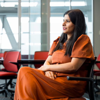 A woman in an orange dress seated on a red chair, speaking to an interviewer