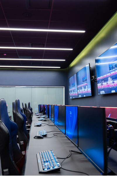 A modern cyber range room featuring multiple high-end gaming PCs with ergonomic chairs and large monitors.