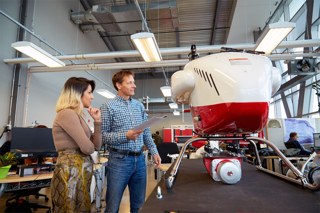 Two RPAS professionals discuss a large prototype of a large drone in a modern workspace. The environment features technology and collaborative efforts in engineering.
