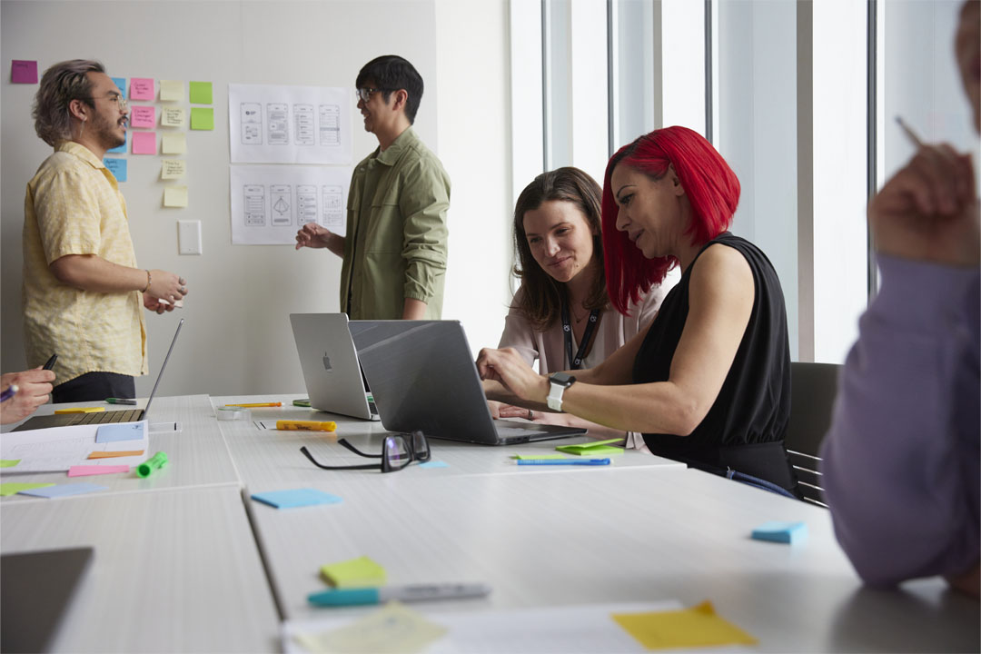 A collaborative workspace where interactive design students are engaged in a meeting, discussing ideas and working on laptops.