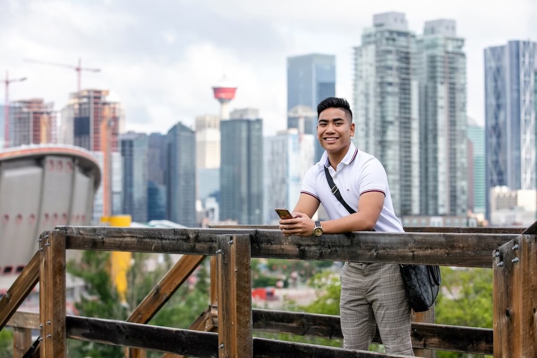 A student stands outside with downtown Calgary in the background