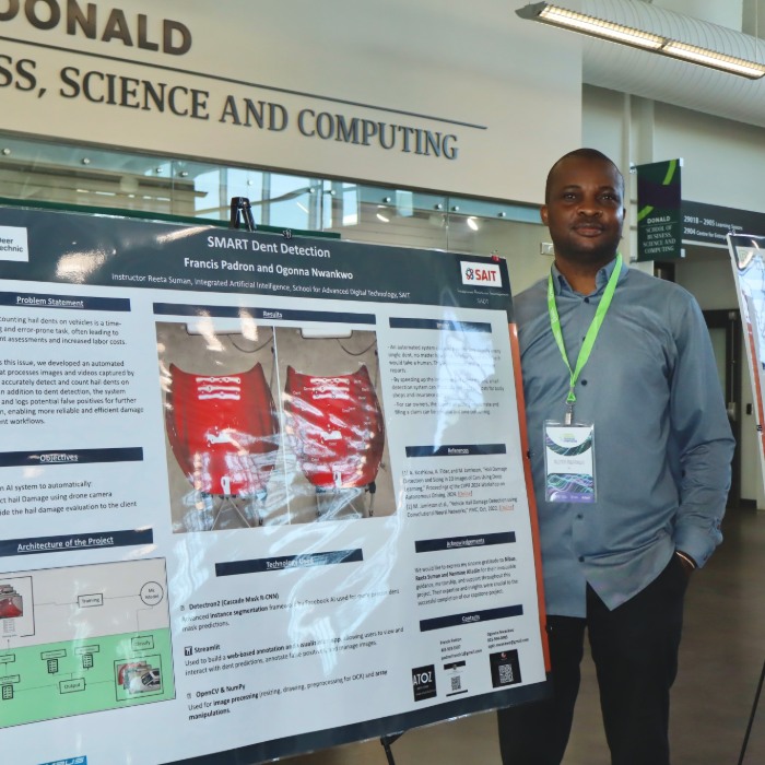 Student standing with research poster, smiling.