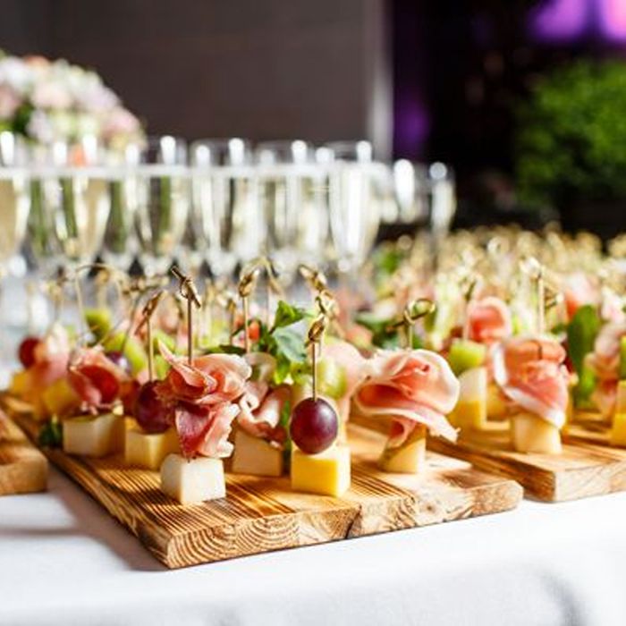 Assorted appetizer skewers on wooden boards with champagne glasses in the background.