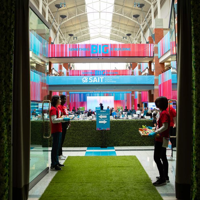 SAIT atrium with colorful banners, event booths, and staff greeting attendees.