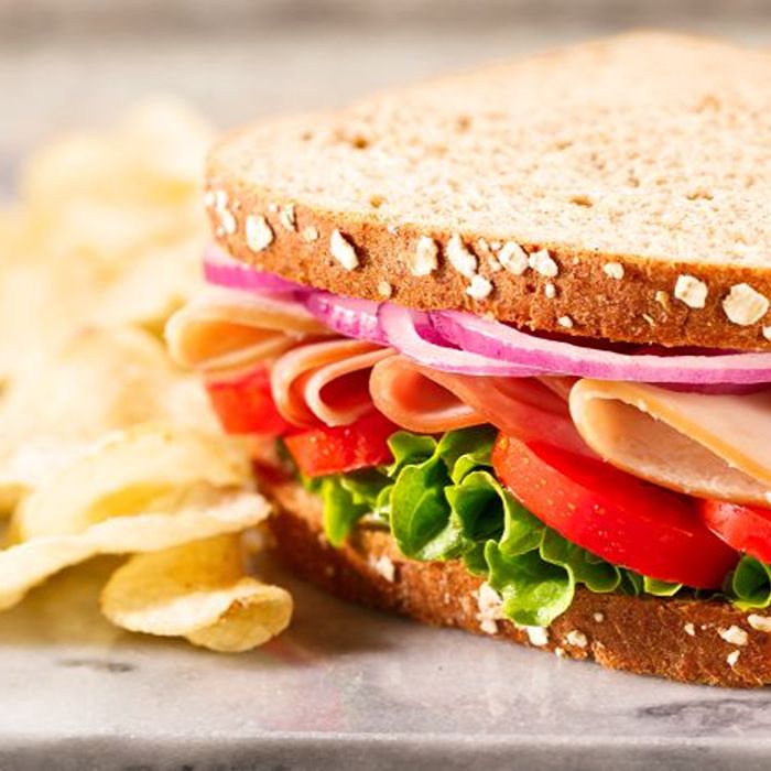 Turkey sandwich with lettuce and tomato served beside potato chips.