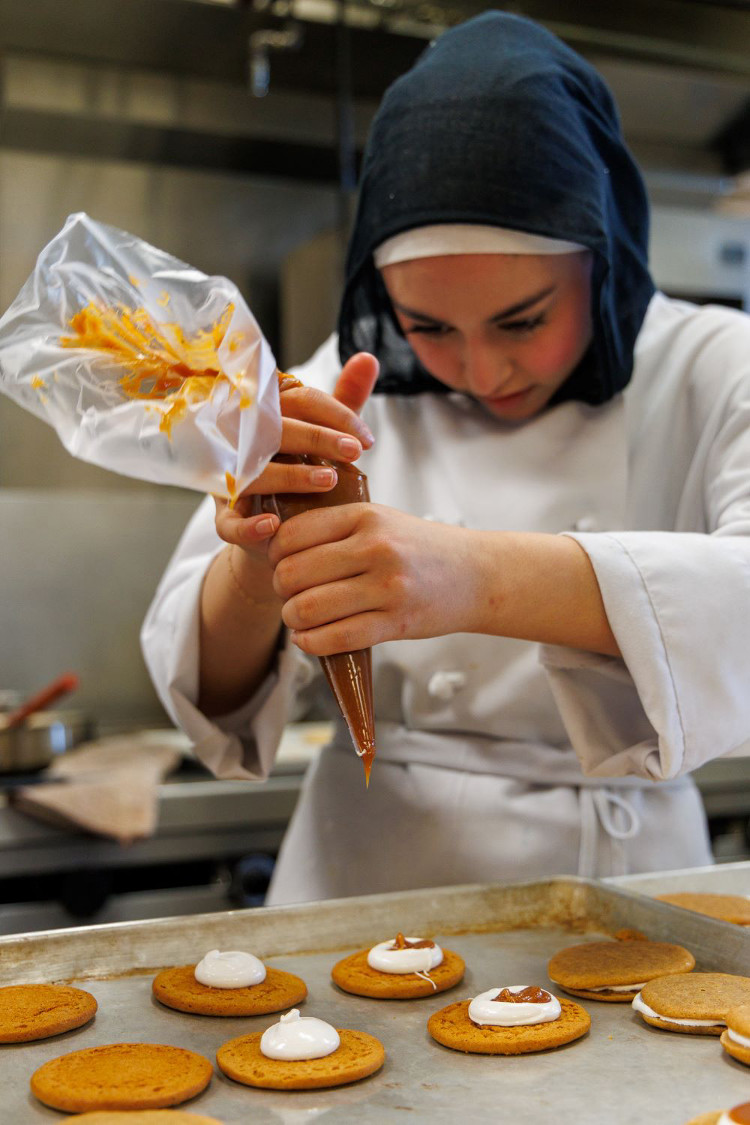 Student piping caramel and cream onto round cookies