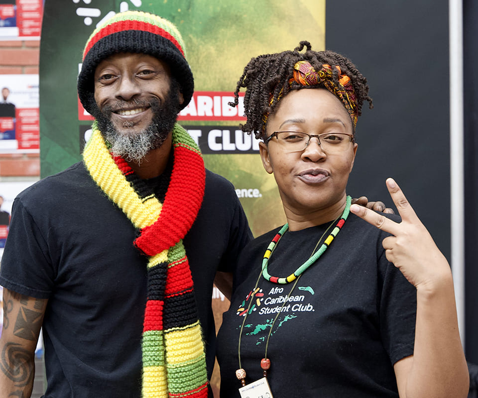 Two individuals pose together wearing vibrant colors inspired by Rasta culture at a booth for the Afro Caribbean Student Club.