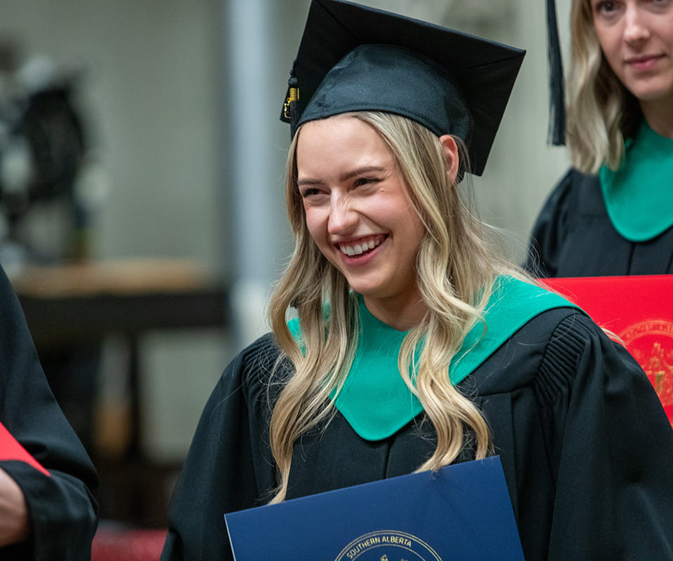 Smiling graduate in cap and gown holding diploma celebrating a significant accomplishment.