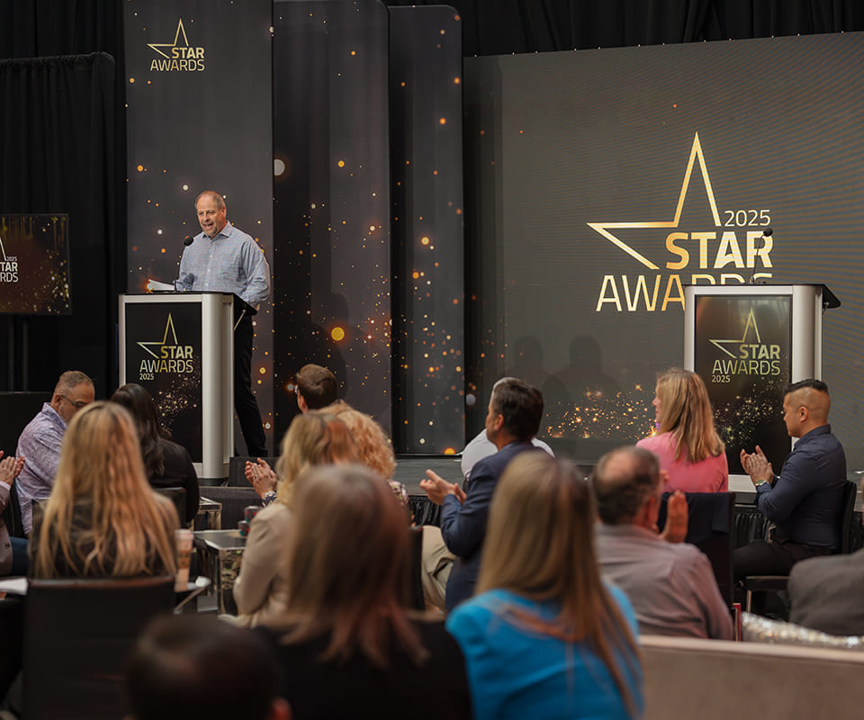 Speaker presenting at the 2025 STAR Awards ceremony with an audience engaged and a backdrop featuring the events logo.