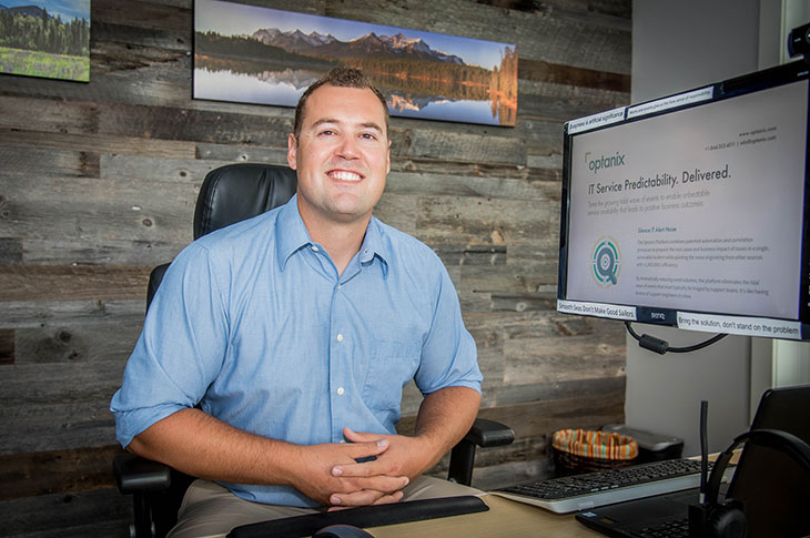 Carl Heikel - caucasian male sitting at desk  wearing khakis and blue dress shirt, short brown hair, smiling towards camera