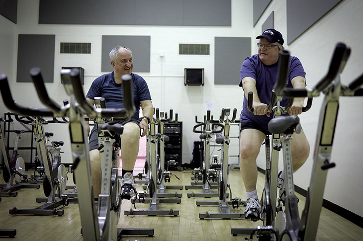 Two Youquest members cycle on stationary bikes in SAIT's cycling room.