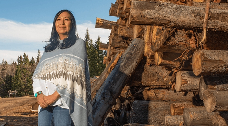 Indigenous woman standing in front of a wood pile at sawmill