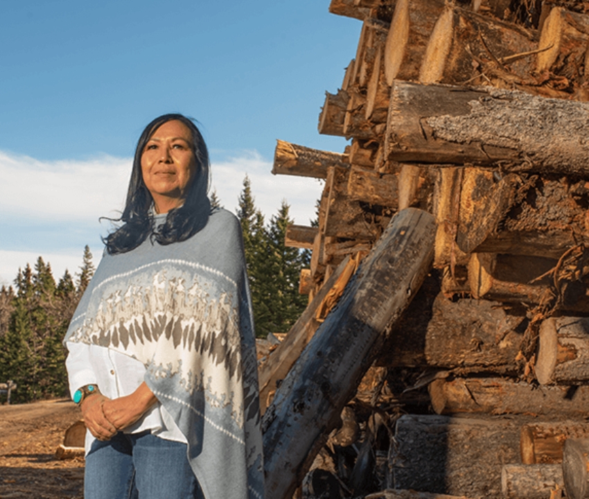 Indigenous woman standing in front of a wood pile at sawmill