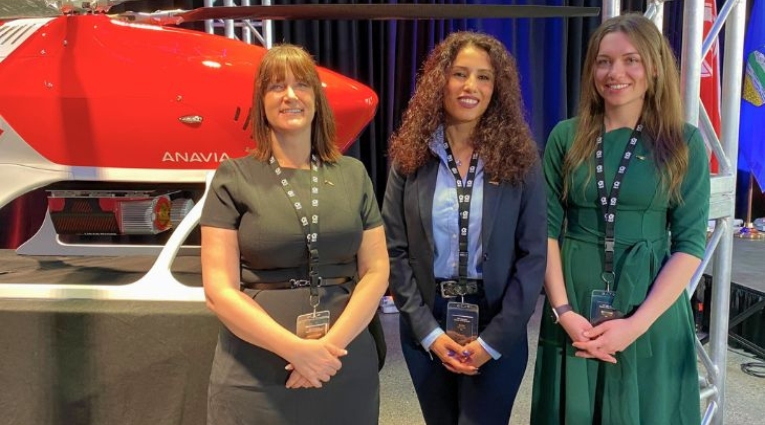 Three females standing and smiling in front of a drone helicopter