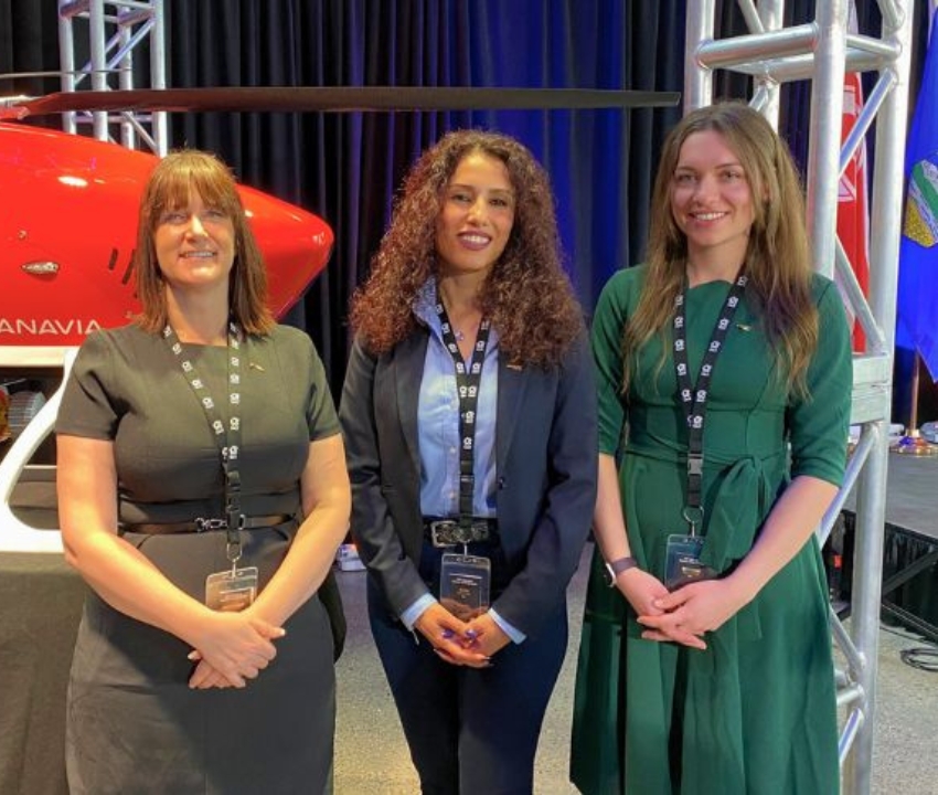 Three females standing and smiling in front of a drone helicopter