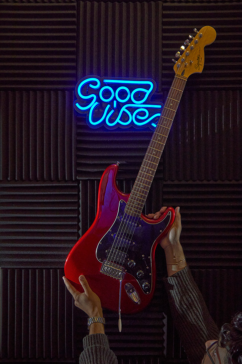 Acoustic guitar being hung up on a way with neon light behind