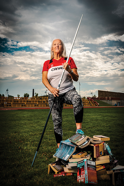 female holding javelin with one foot on a stack of books